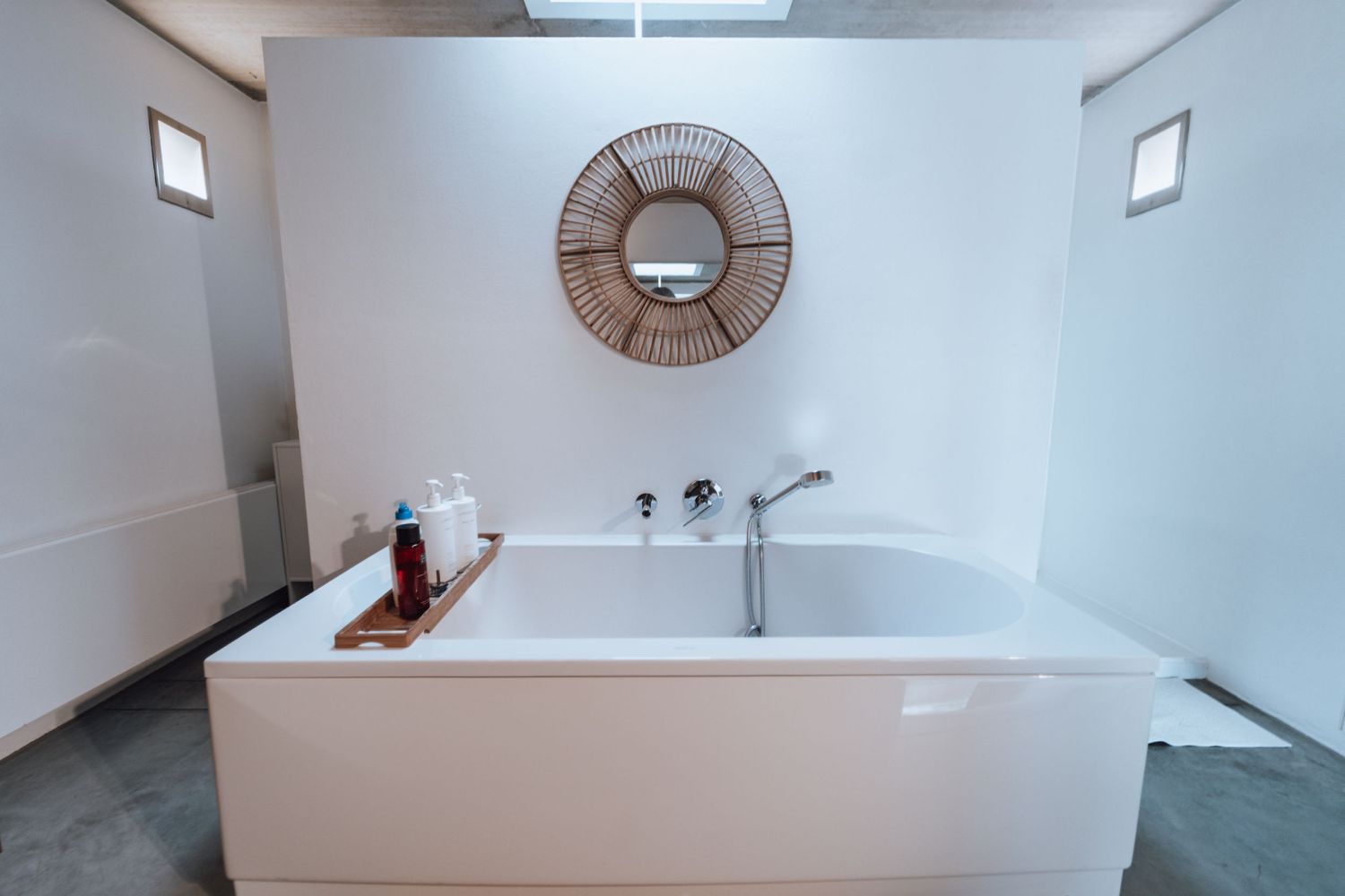 Nette witte badkamer met groot bad en decoratieve ronde spiegel aan de muur.