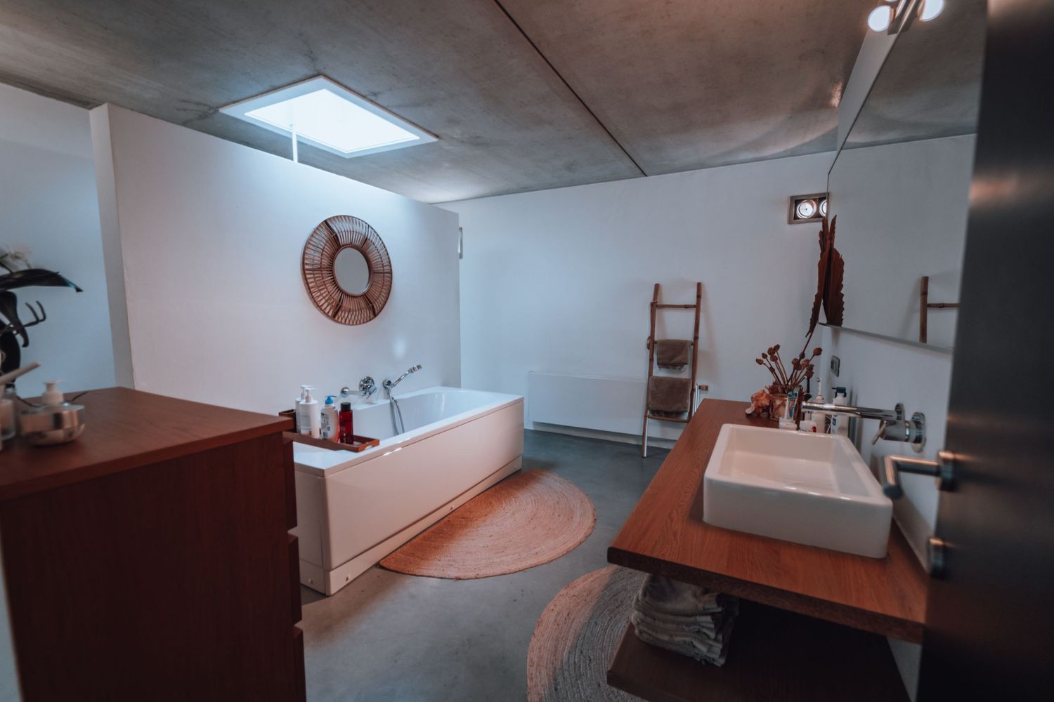 Modern badkamerinterieur met strak houten badmeubel, witte wasbak en luxe hoekbad onder inbouwverlichting.