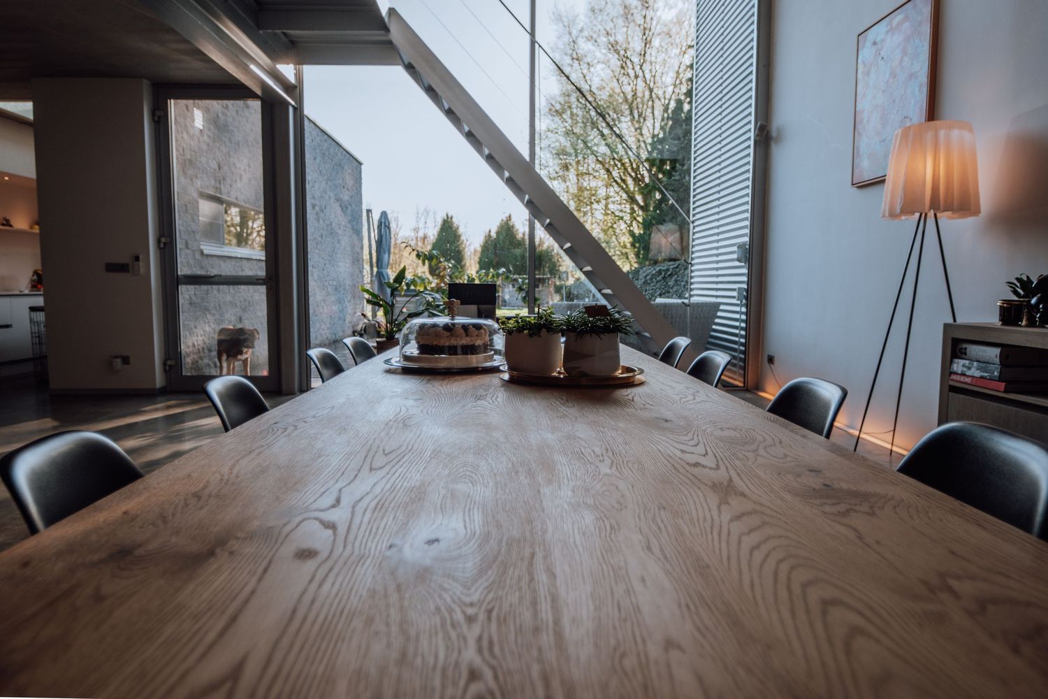 Een moderne eetkamer met een grote houten tafel, zwarte stoelen en natuurlijk licht door ramen van vloer tot plafond.