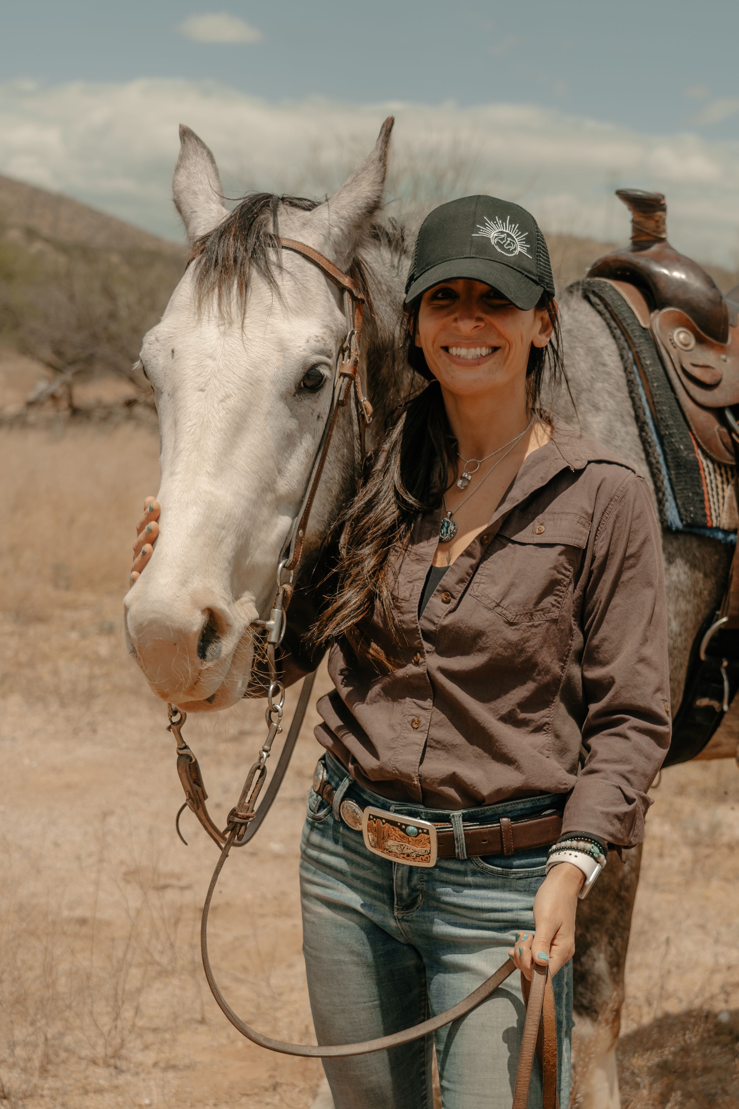 A beautiful white horse with western tack stands next to a rider in casual ranch attire.