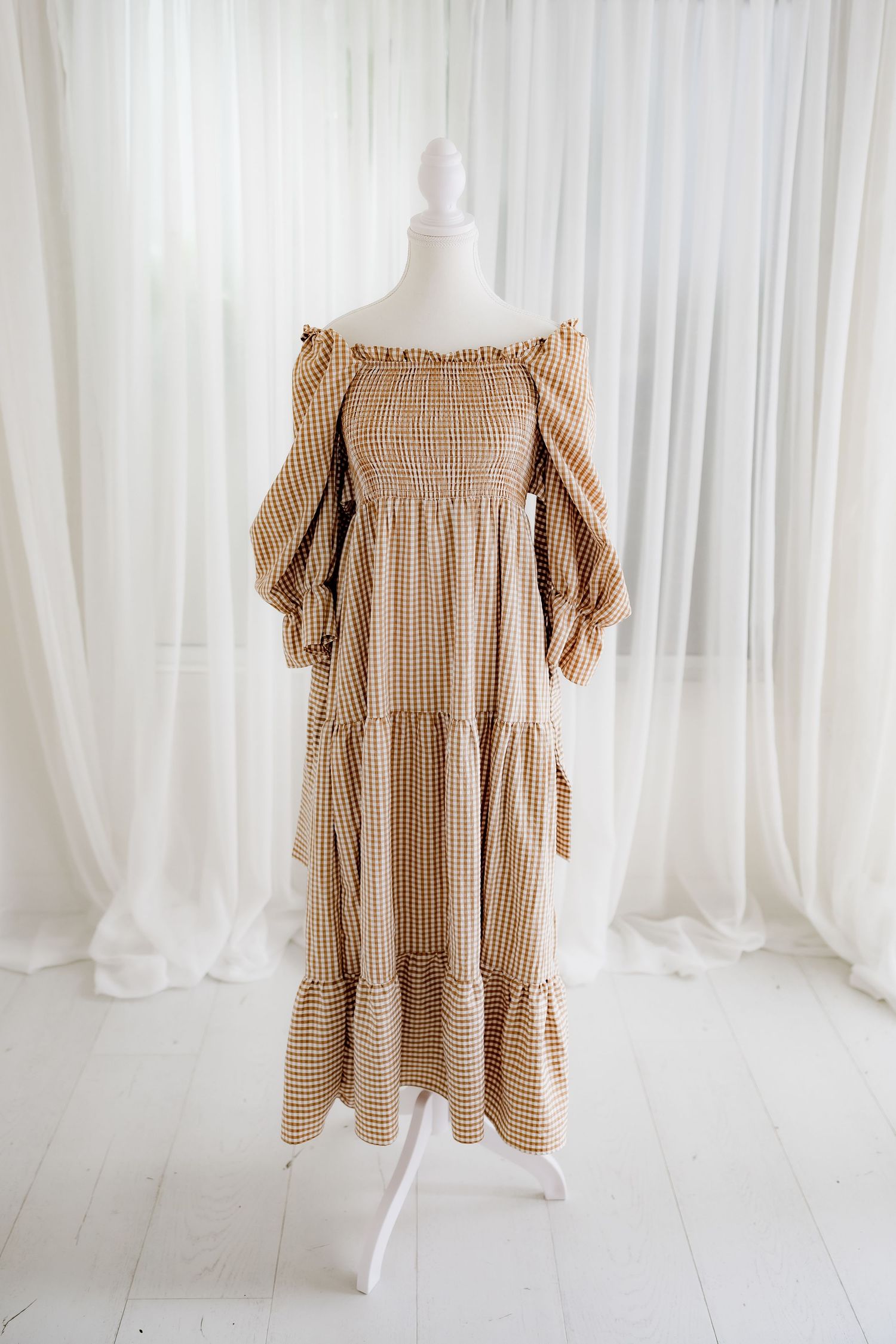 Long brown and white gingham dress with smocked bodice and tiered skirt displayed on white mannequin.