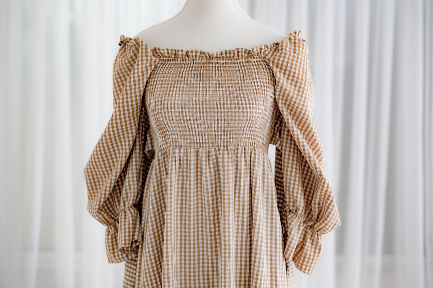 Detailed view of ruffled neckline and smocked bodice on brown gingham prairie dress.