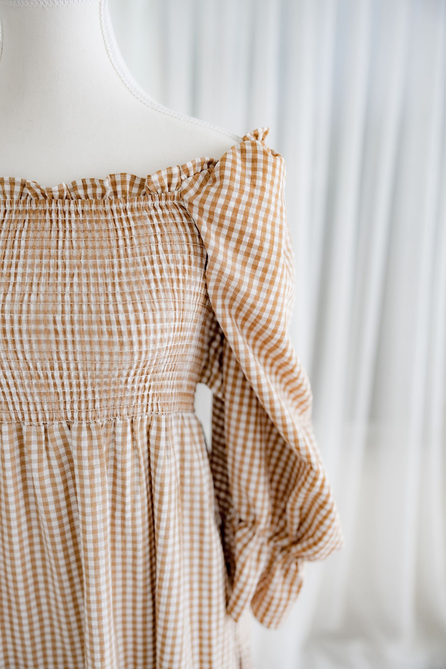 Detailed shot of brown checkered fabric with smocked bodice and ruffle trim.