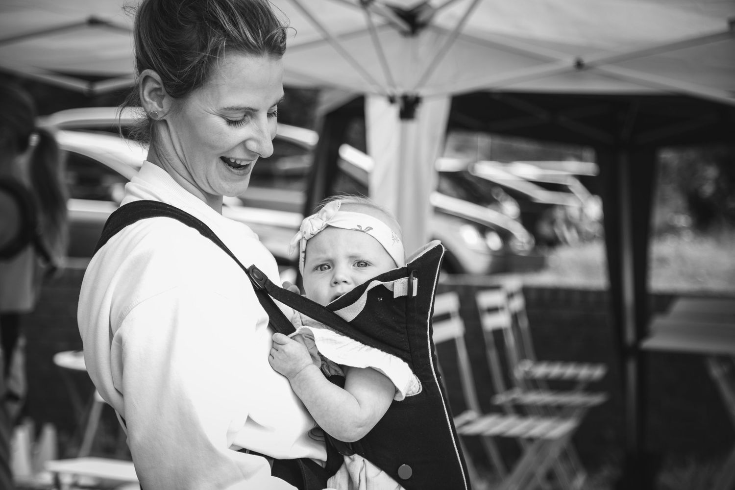 A caregiver wearing a baby carrier smiles during an outdoor event.