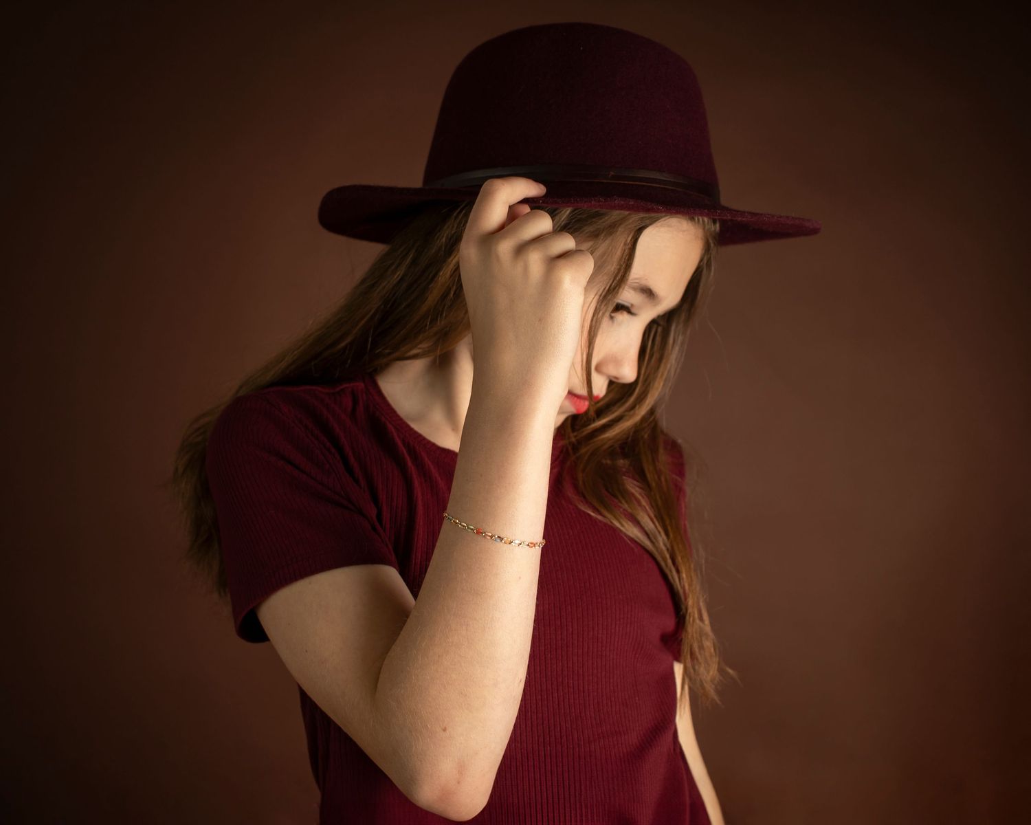 A school-age girl holds her hat brim while looking down and to the right