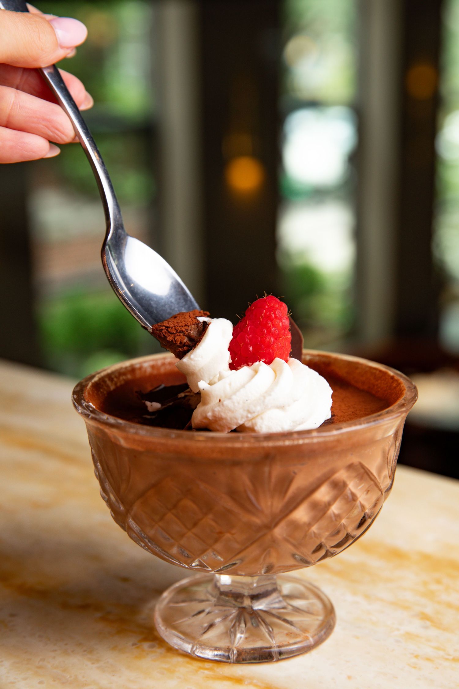 A chocolate mousse dessert topped with whipped cream and fresh raspberry in a crystal dish.