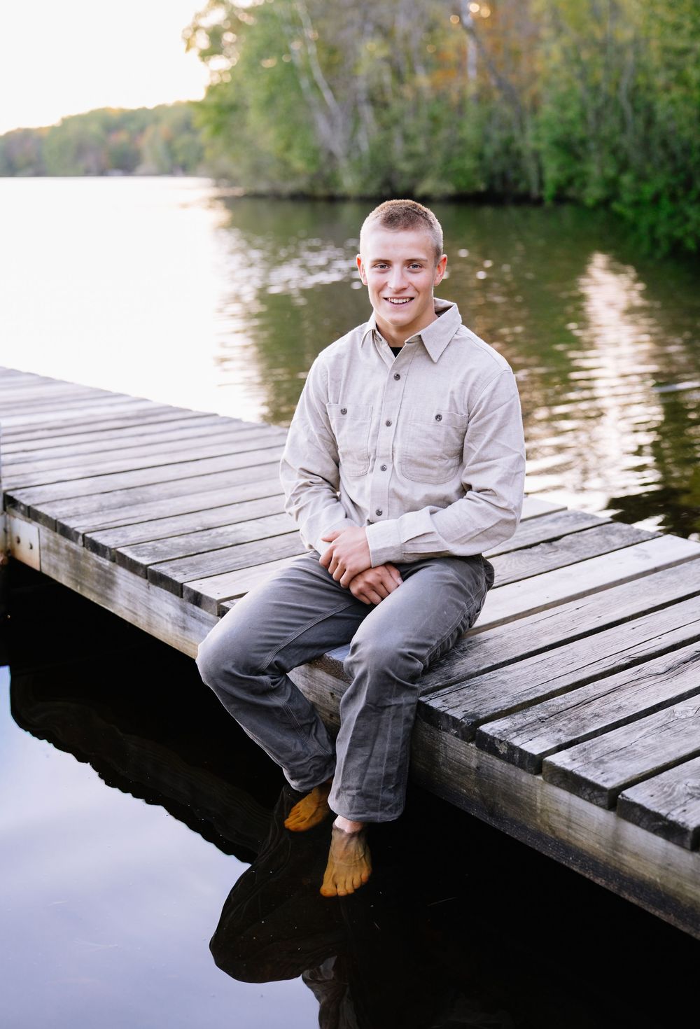Person sitting on wooden dock at sunset wearing casual button-down shirt.