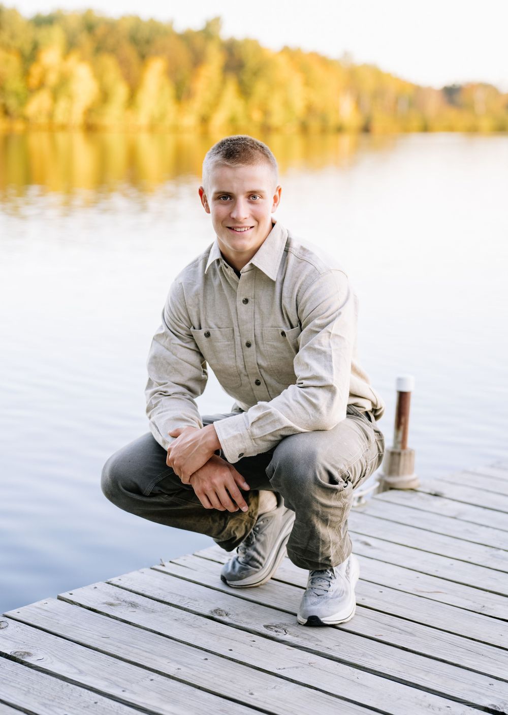 Person crouching on wooden dock over calm lake at golden hour.