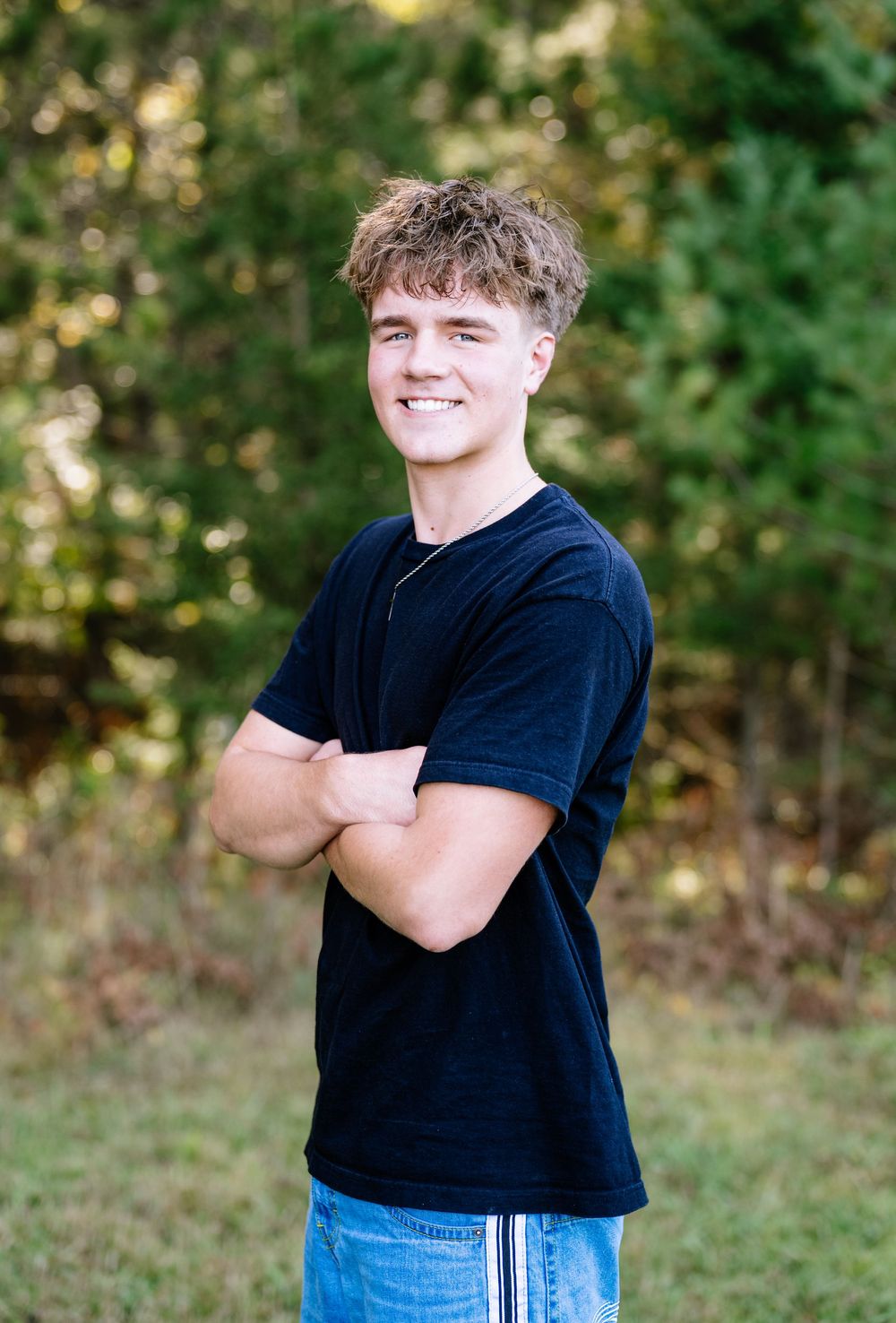 Portrait of someone in a navy t-shirt with curly hair against a natural outdoor background.