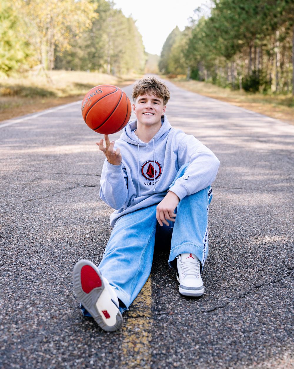 Person in light blue hoodie sitting on road spinning basketball on finger.