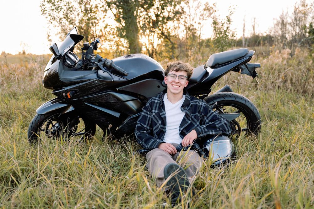 Person relaxes beside black motorcycle in tall grass during golden hour.