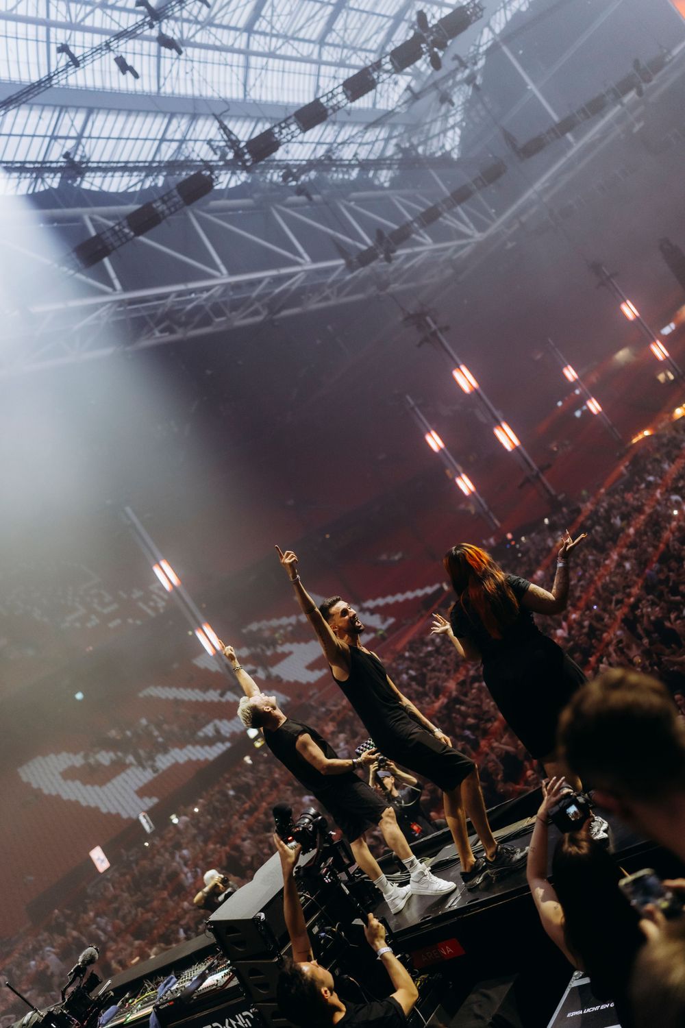 Silhouettes of performers on stage with dramatic lighting and crowd in foreground.