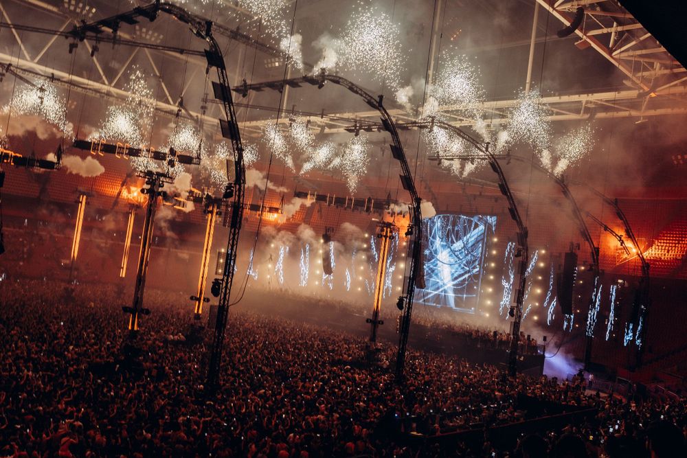 Festival stage with pyrotechnics and light shows creating dramatic atmosphere over crowd.