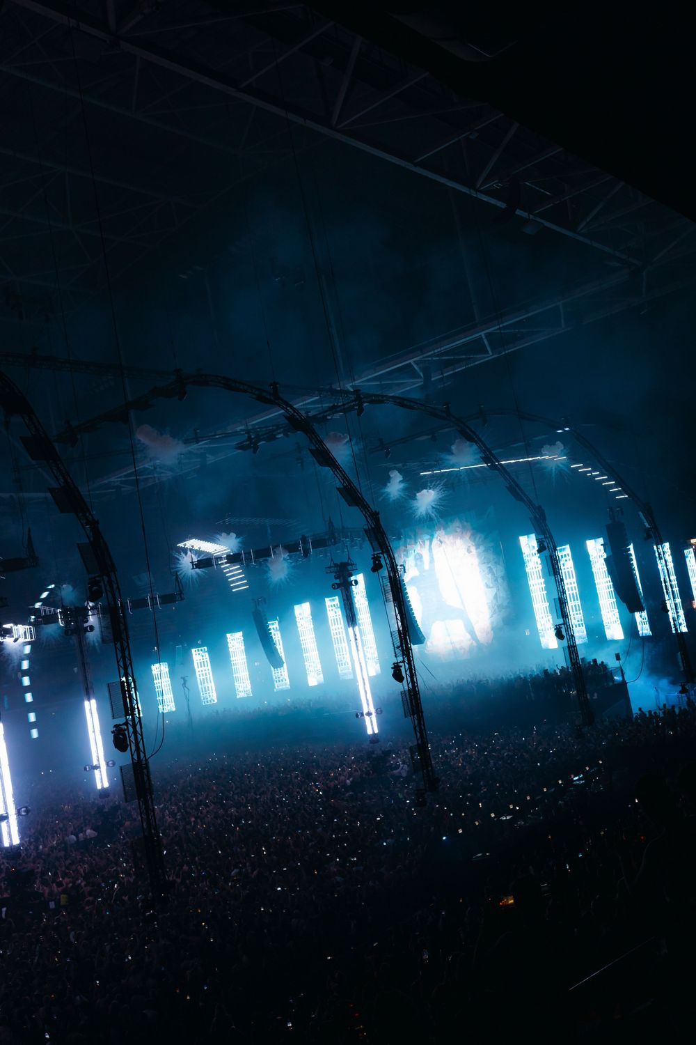 Concert venue with blue vertical LED light pillars and atmospheric fog effects.