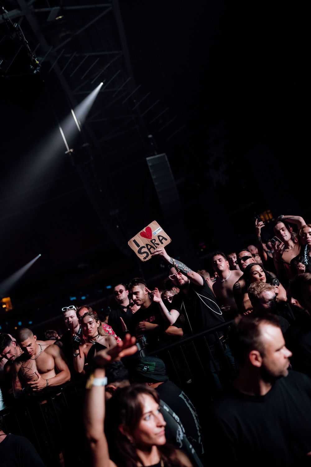Dark concert venue filled with enthusiastic fans reaching towards the stage.