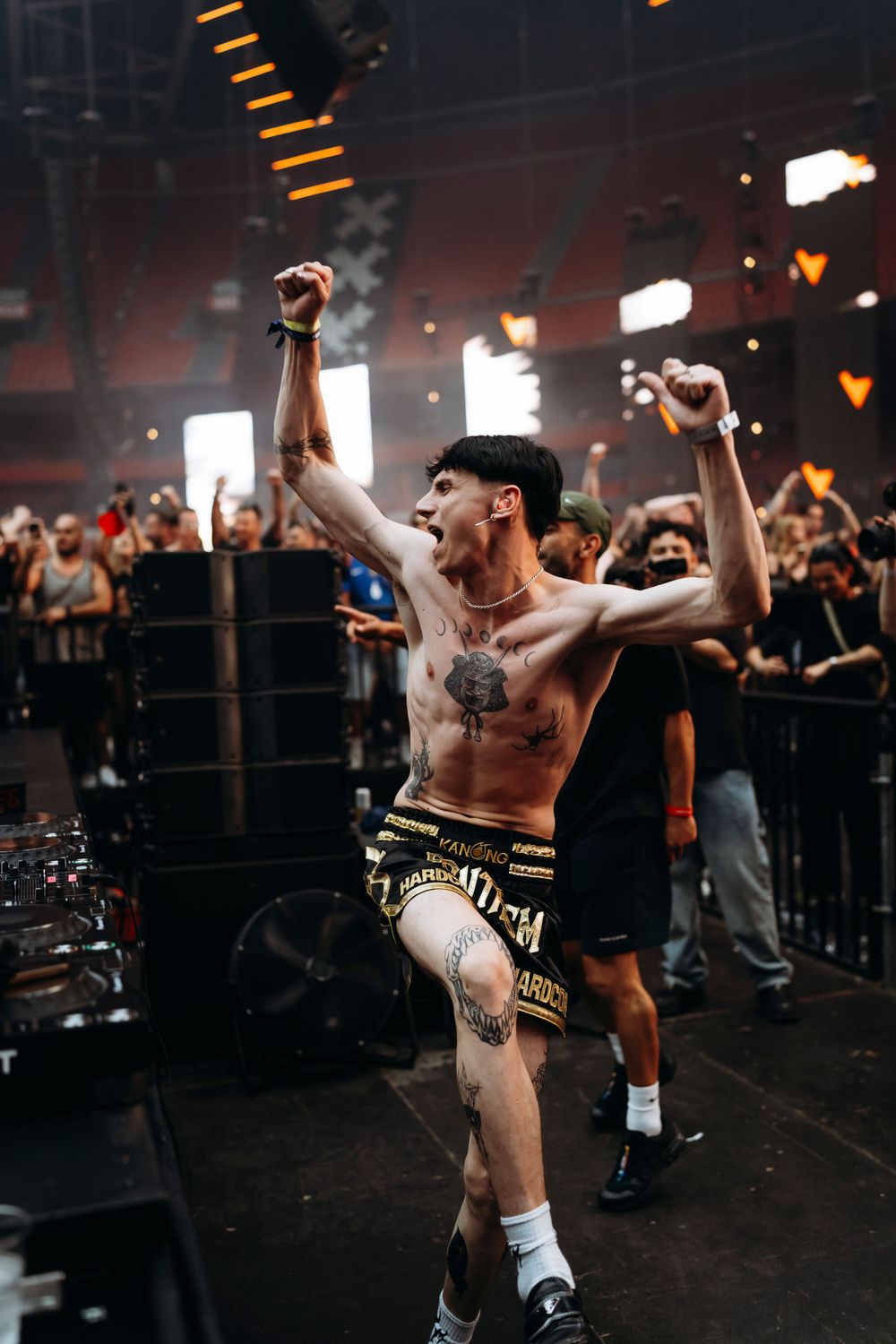 Energetic performer dancing shirtless on stage at indoor venue.