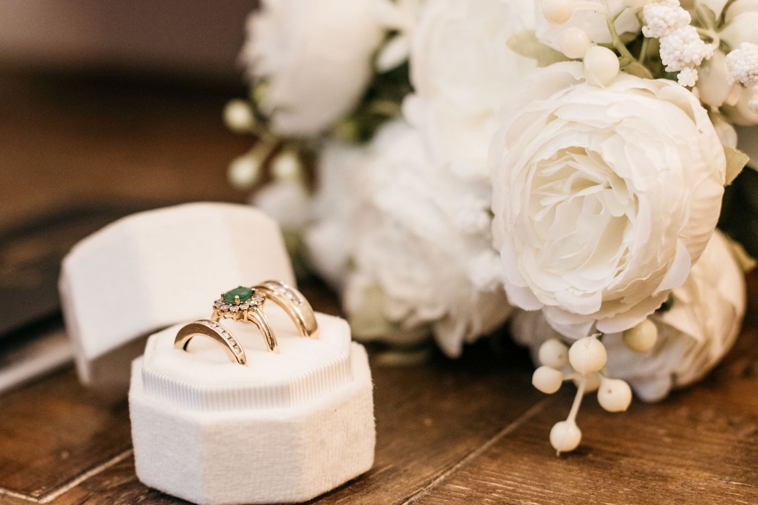 Wedding rings displayed in a white ring box with white roses and floral decor.