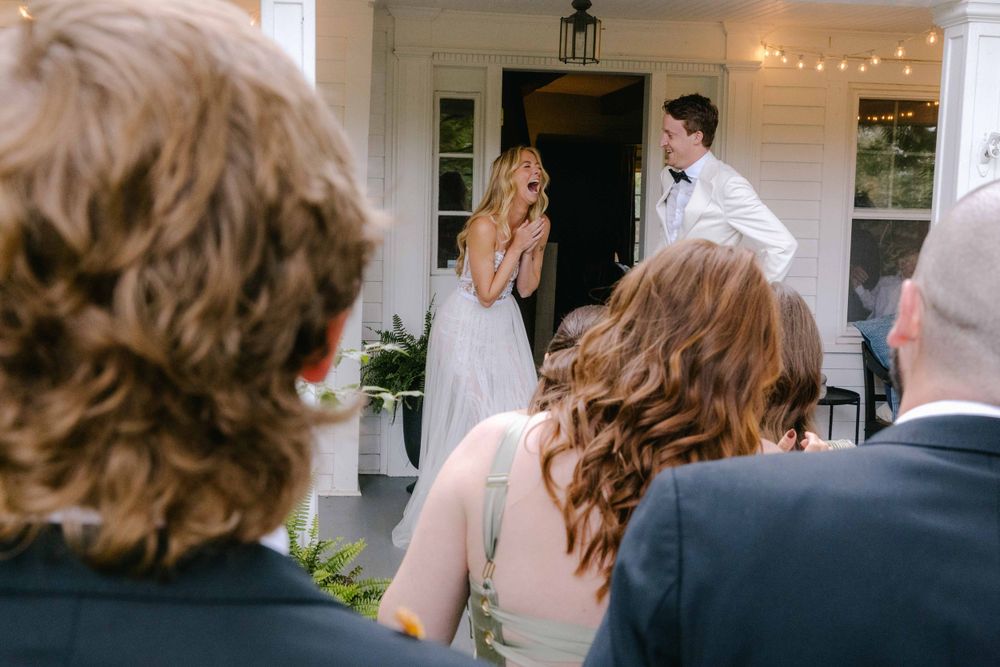 Wedding guests watch couple's first dance through doorway on porch with string lights.