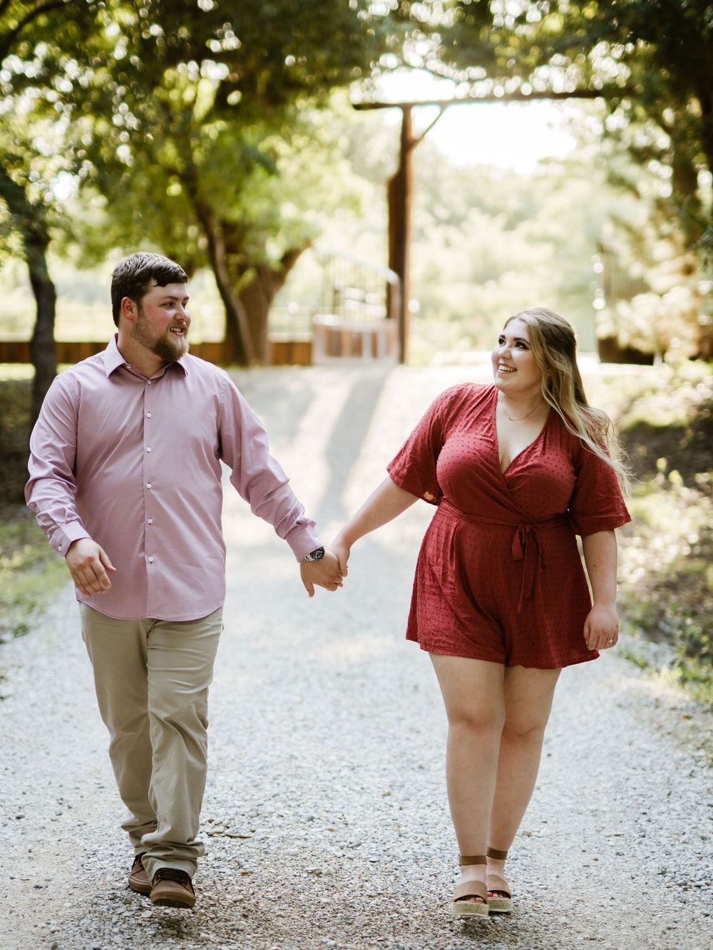 A couple in pink and red outfits walks hand in hand down a scenic country path.