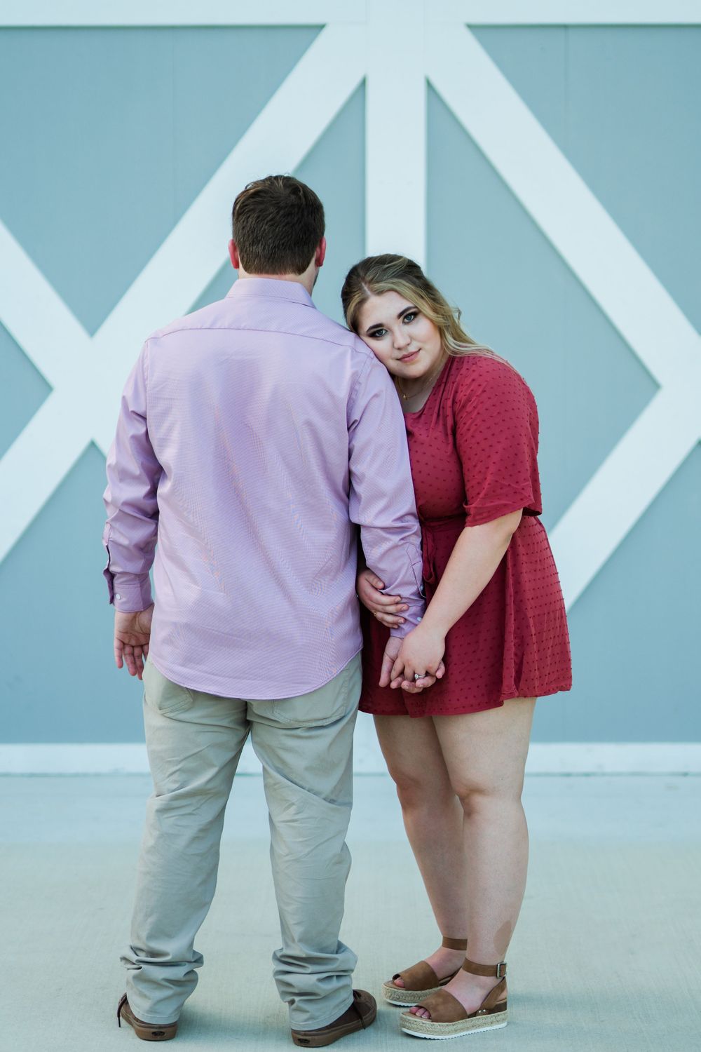 A couple in coordinating pink and red outfits pose together against a blue and white geometric wall.