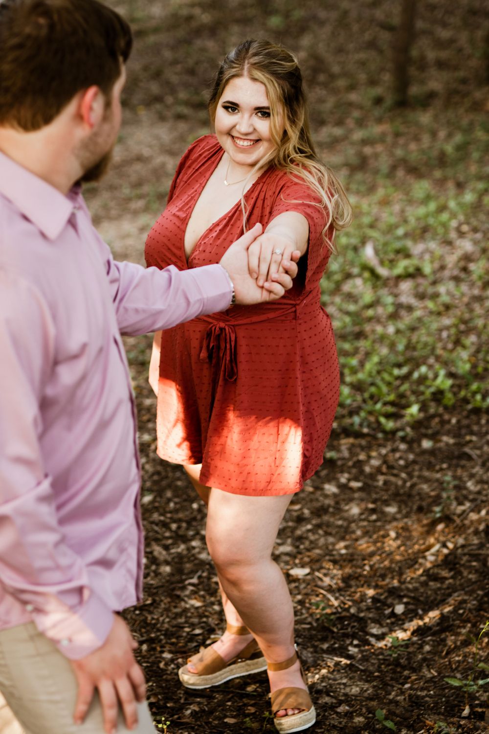 A sweet couple holds hands and dances together on a wooded path.
