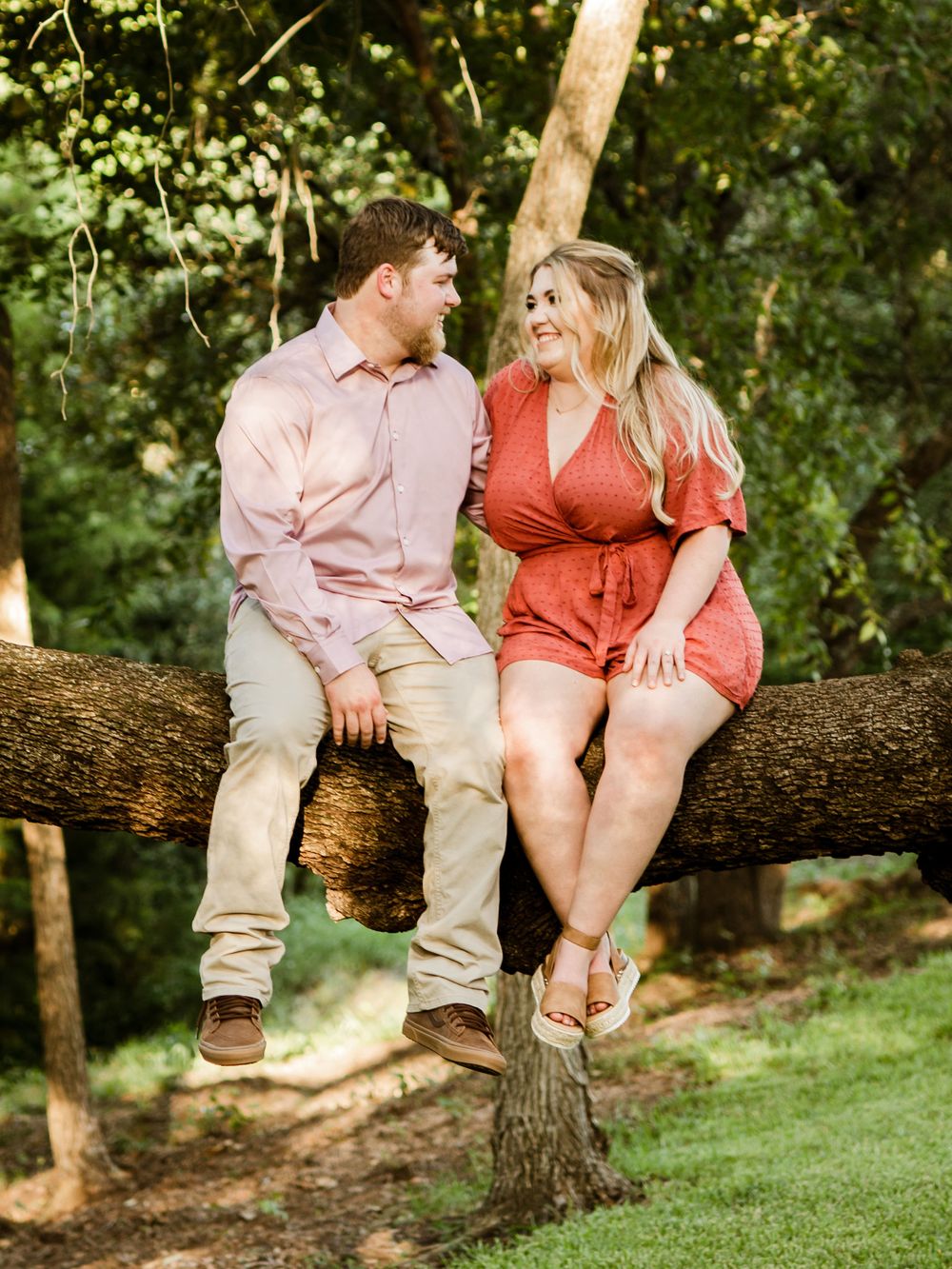 A couple sits together on a fallen tree trunk in a scenic wooded setting.