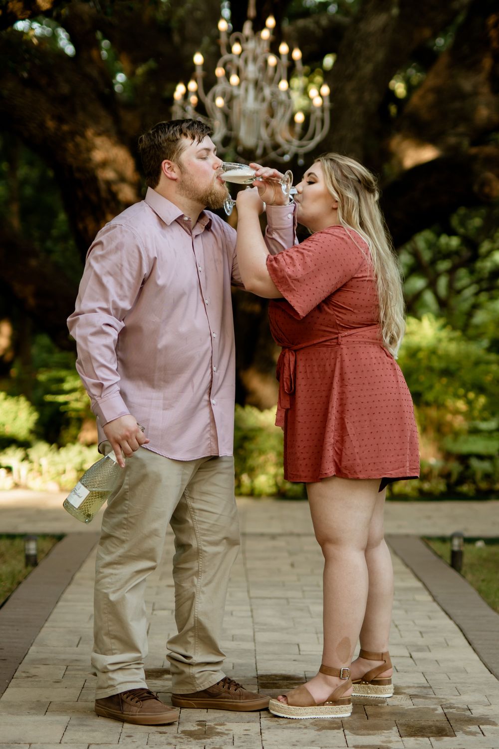 A fun couple shares drinks together under an elegant chandelier in an outdoor setting.
