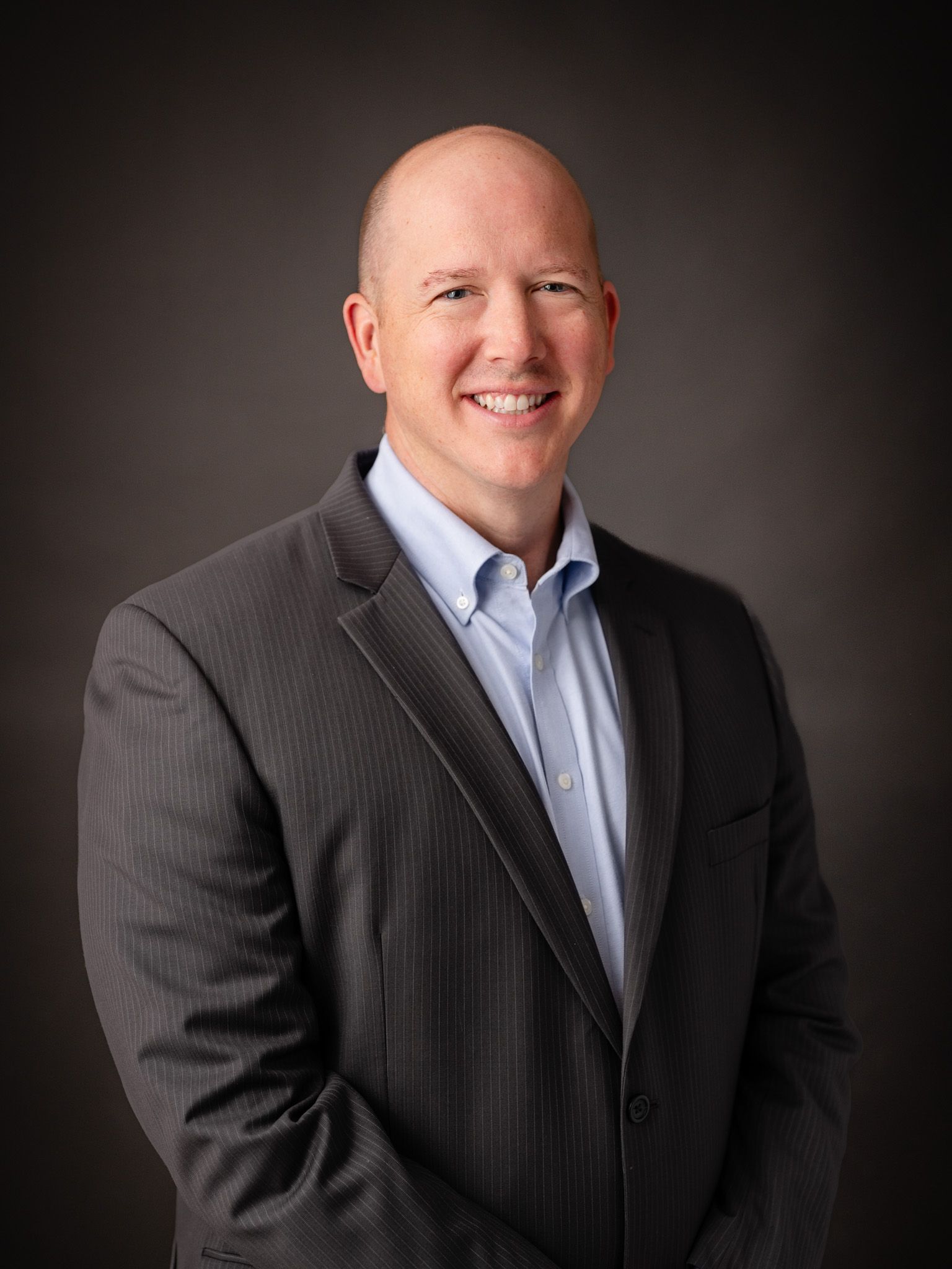 Professional business portrait against dark background with dramatic lighting.
