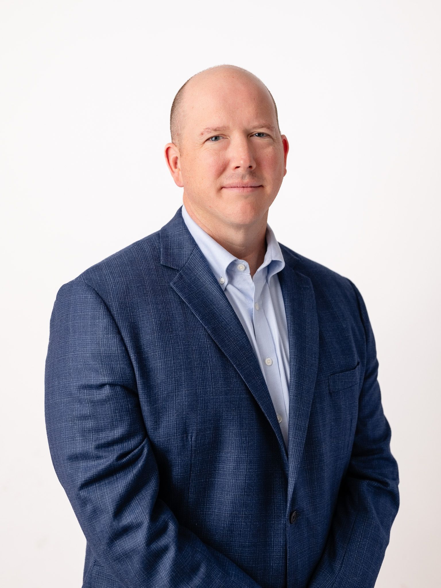 Professional business headshot of person wearing navy blazer against white background.