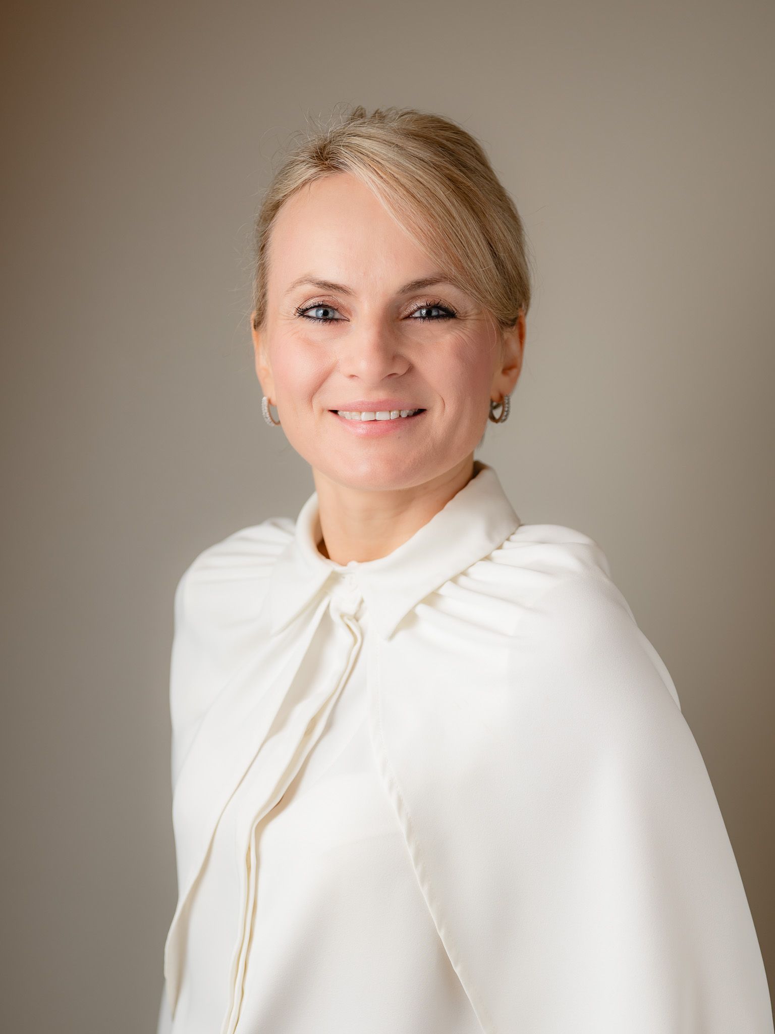 Professional headshot of person wearing white blazer against neutral background.