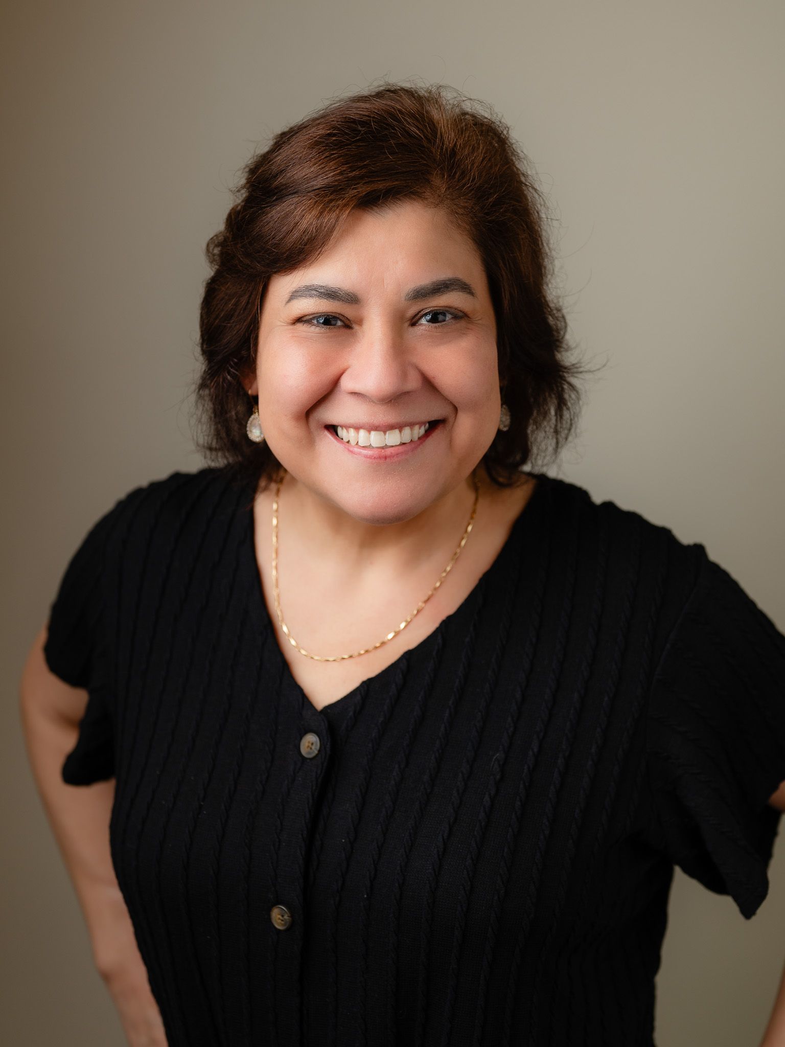 Professional headshot of person wearing black sweater against neutral background.