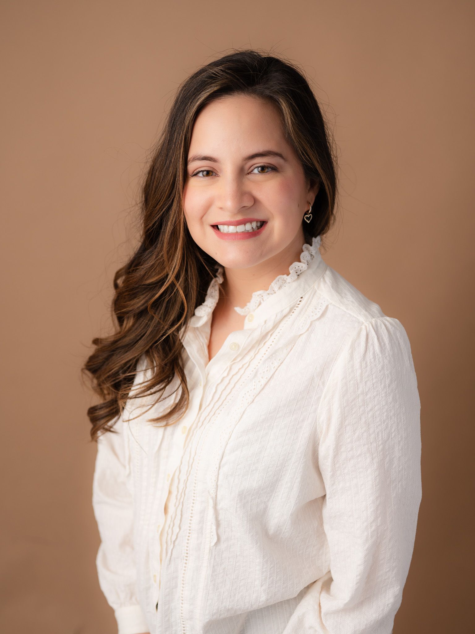 Professional portrait of person in white textured blouse against warm neutral background.