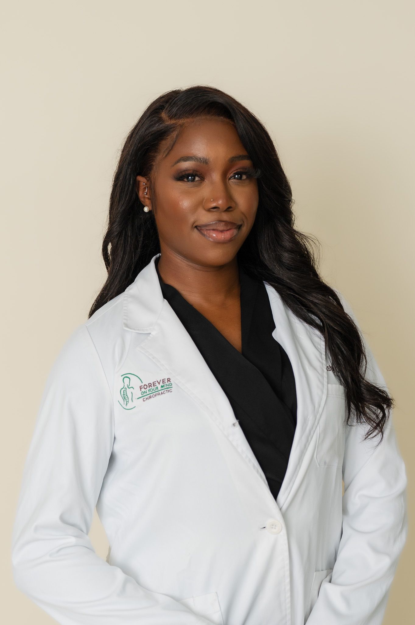 Professional healthcare worker wearing white medical coat and black scrubs against neutral background.