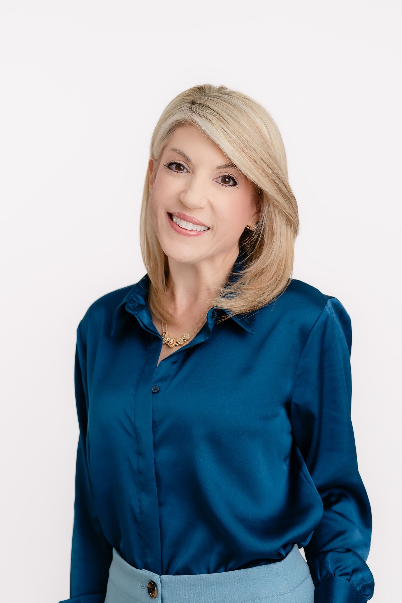 Professional woman in navy blue silk blouse poses for headshot against white background.