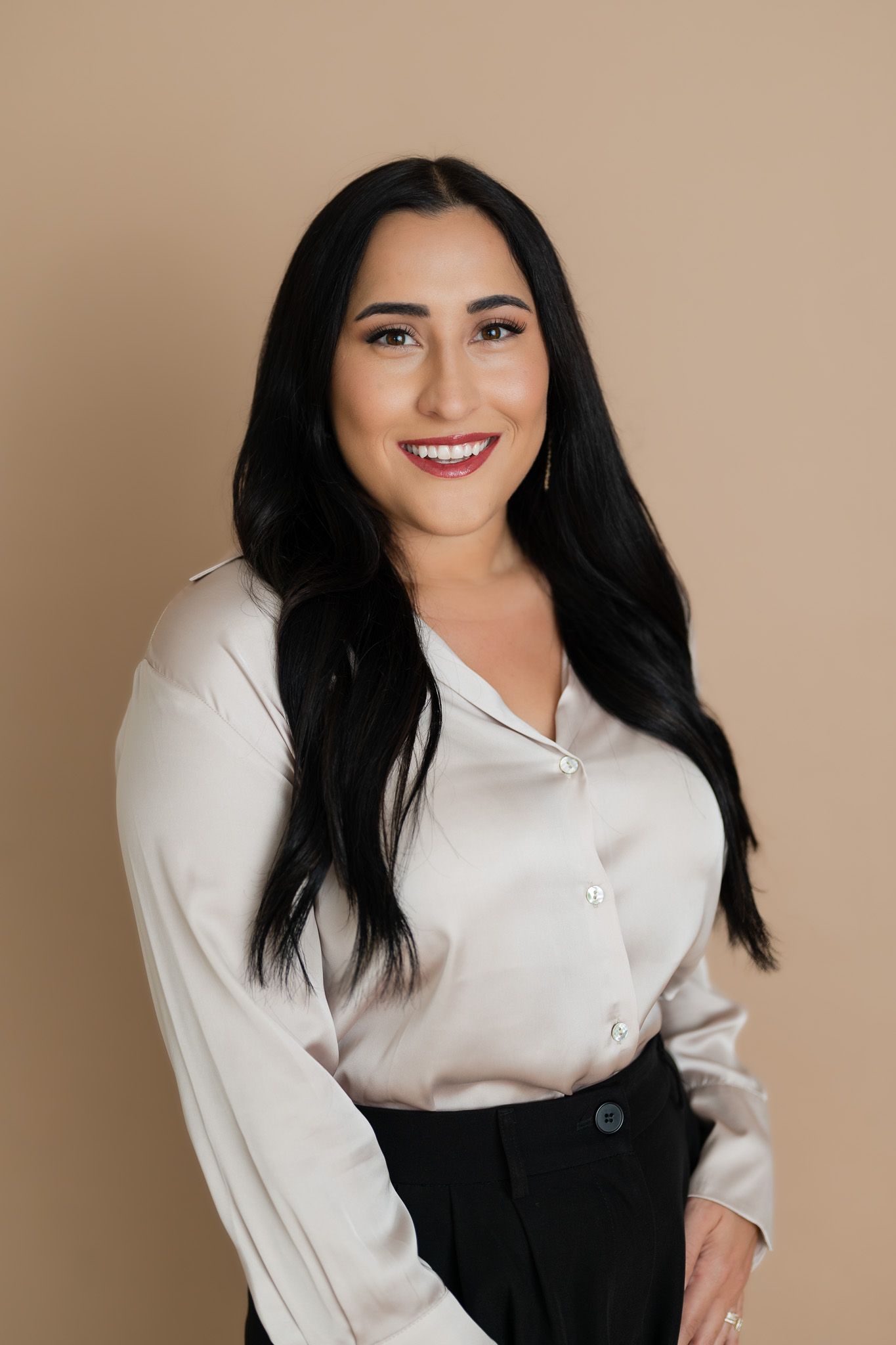 Professional woman in cream colored blouse and dark skirt poses against beige backdrop.