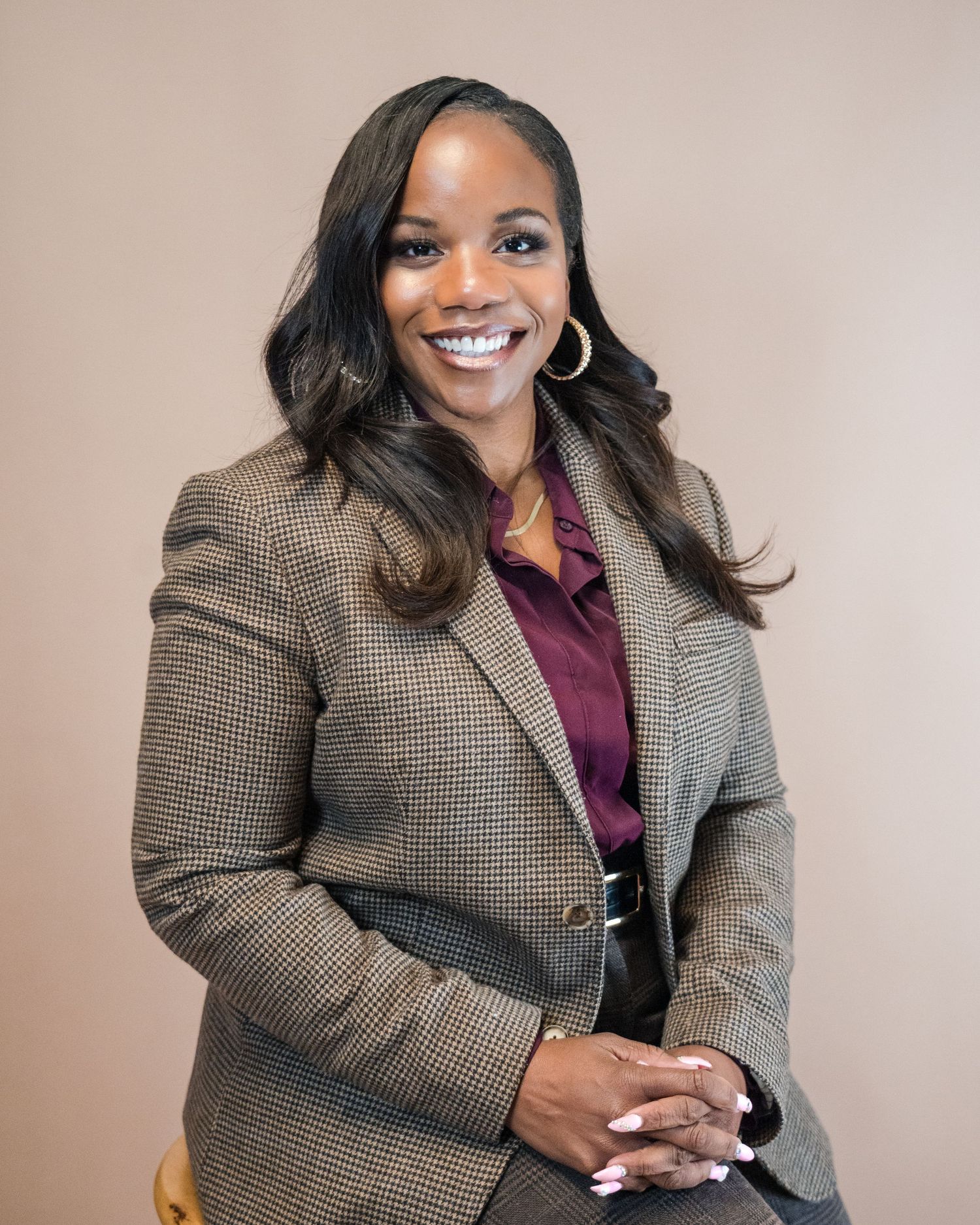 Professional headshot wearing tweed blazer and burgundy top against neutral background.
