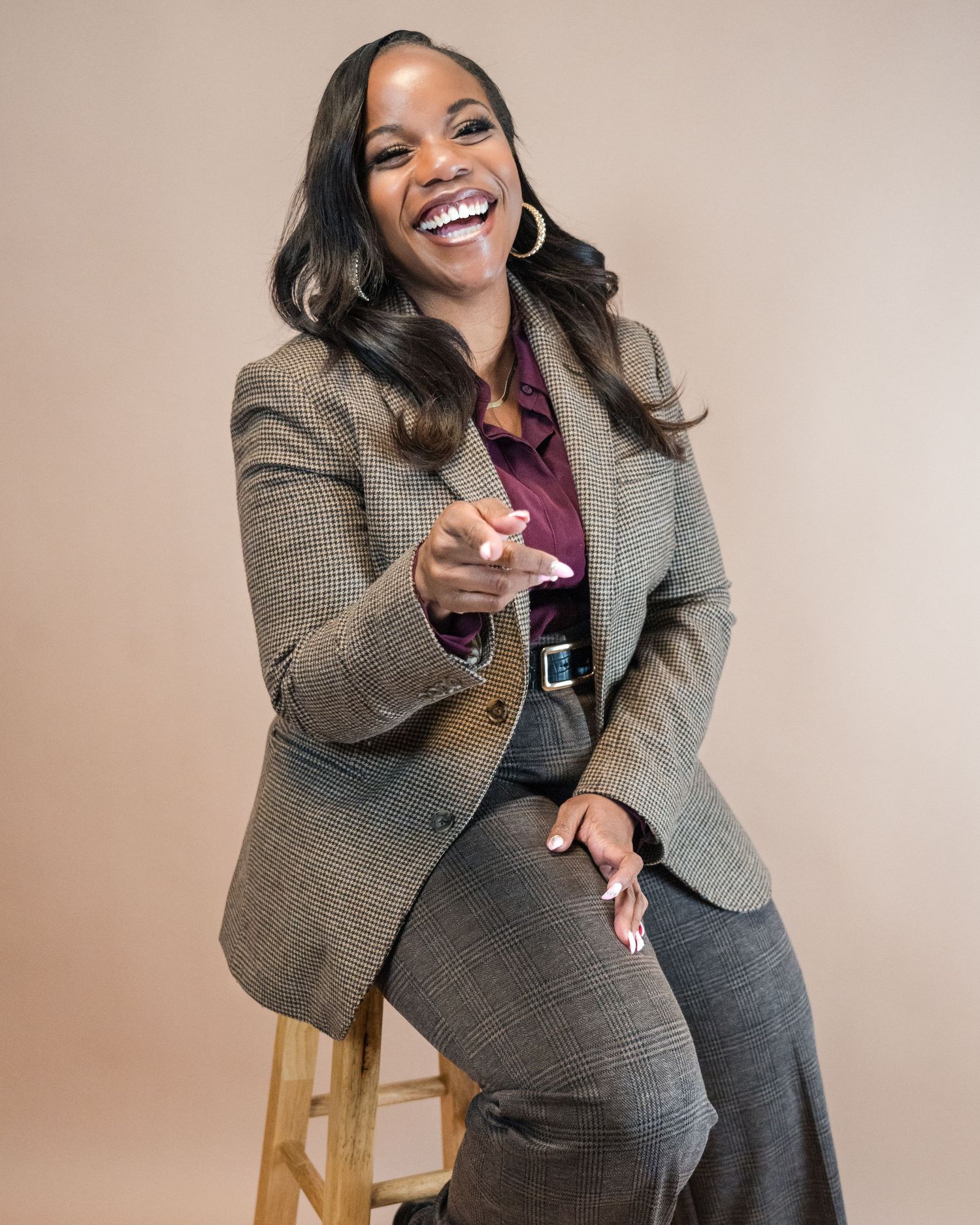 Candid studio portrait in tweed suit sitting on stool with joyful expression.