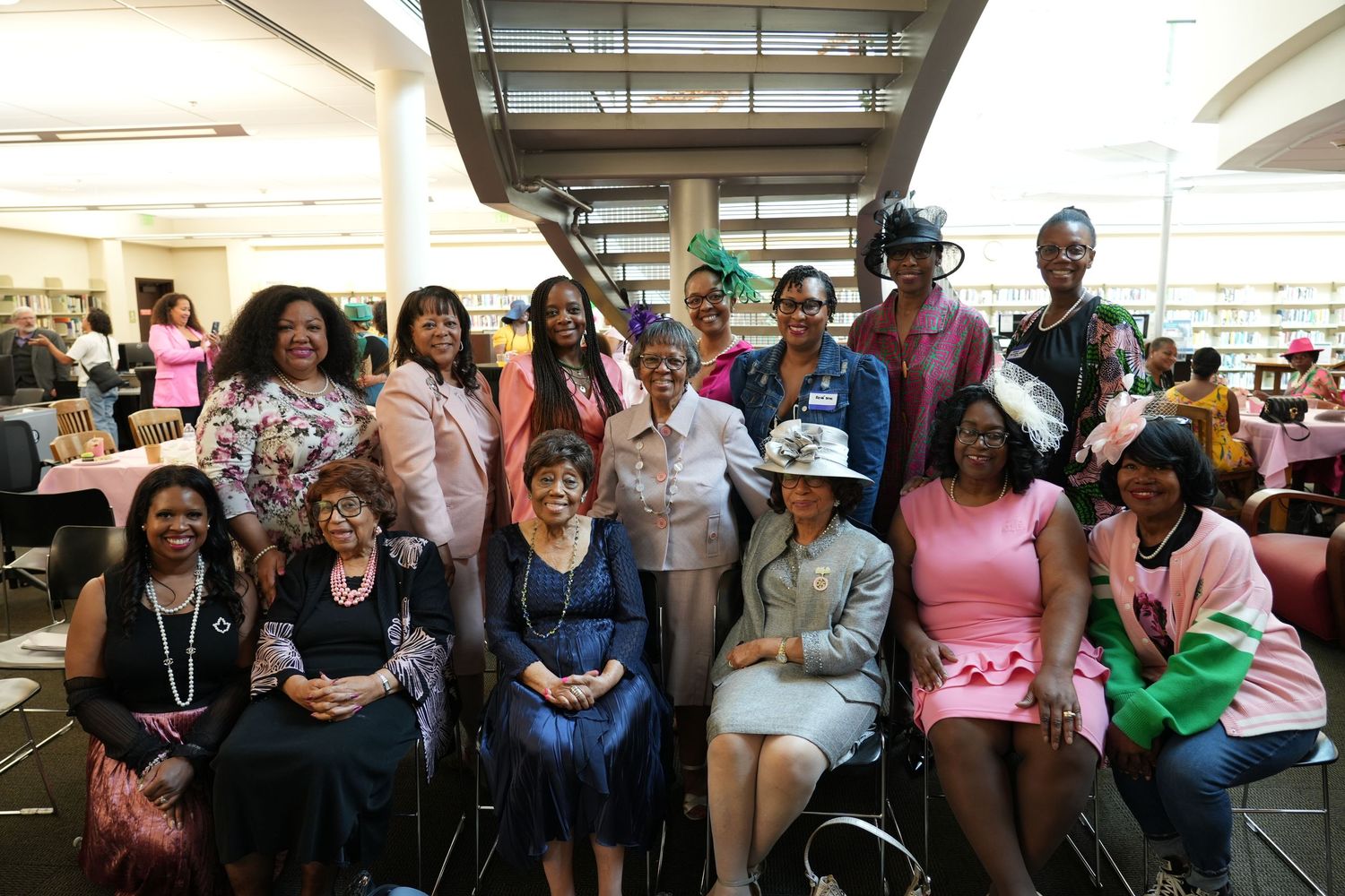 A diverse group of people gather together smiling for a group photo in what appears to be a community center or library setting.