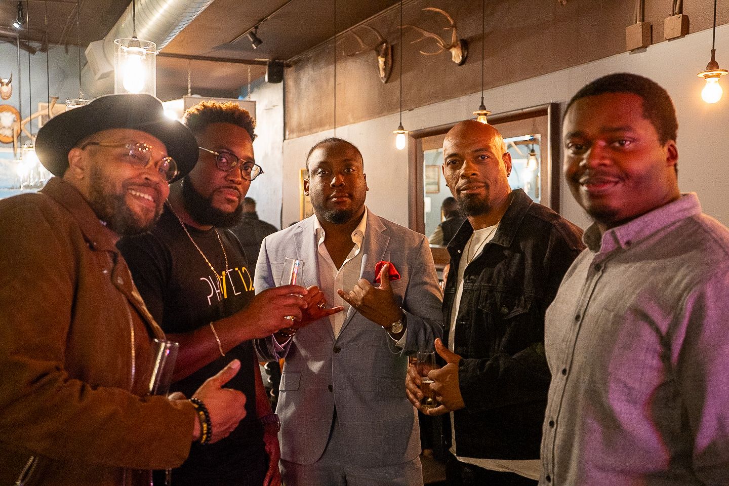 A group of five men gathered together in a warm-lit indoor space, smiling and socializing.