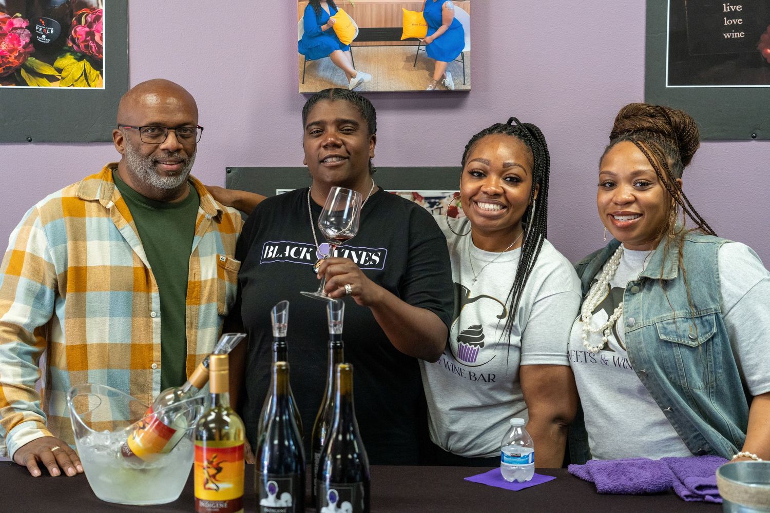 Four staff members smile together behind a counter with wine bottles and glassware at a tasting event.
