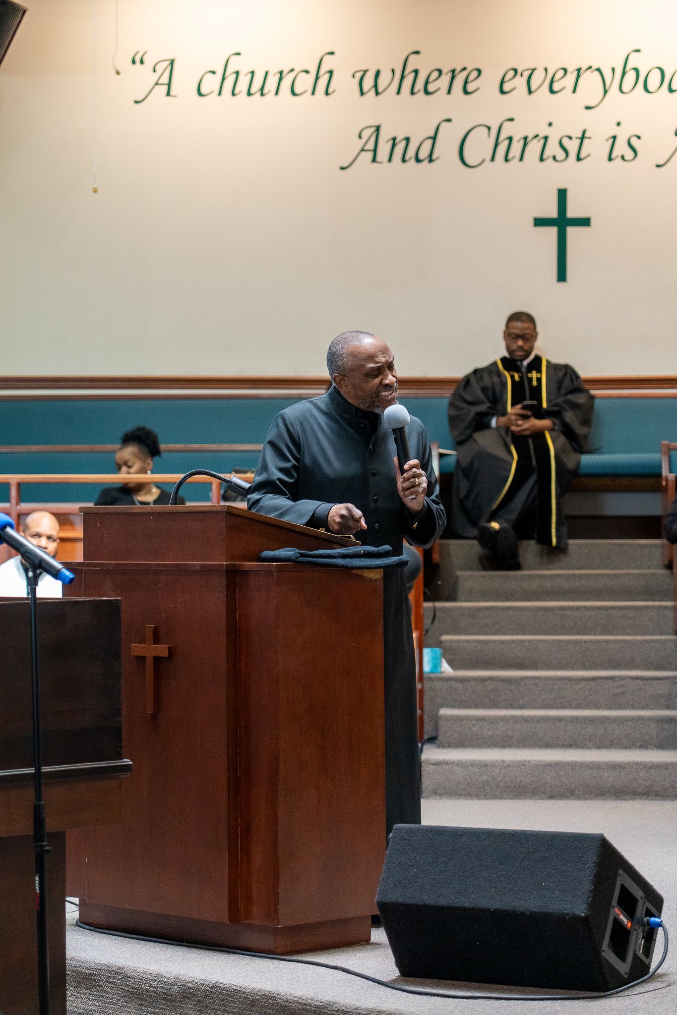 People gathered in a modern church sanctuary with wood paneling and tiered seating during what appears to be a service.