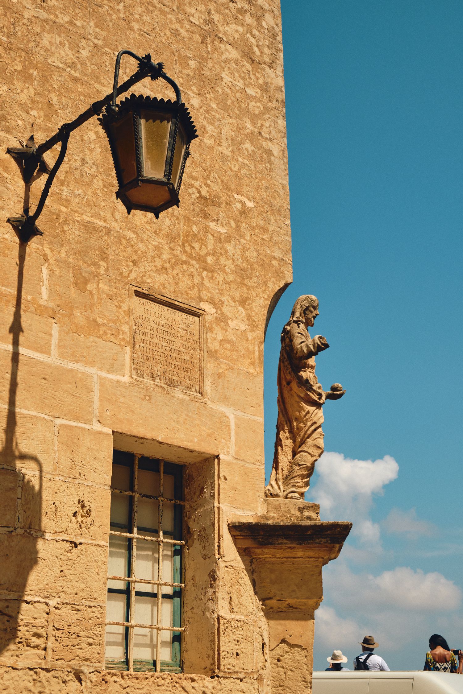 Stone statue and vintage lamp on historic building facade against bright blue sky.
