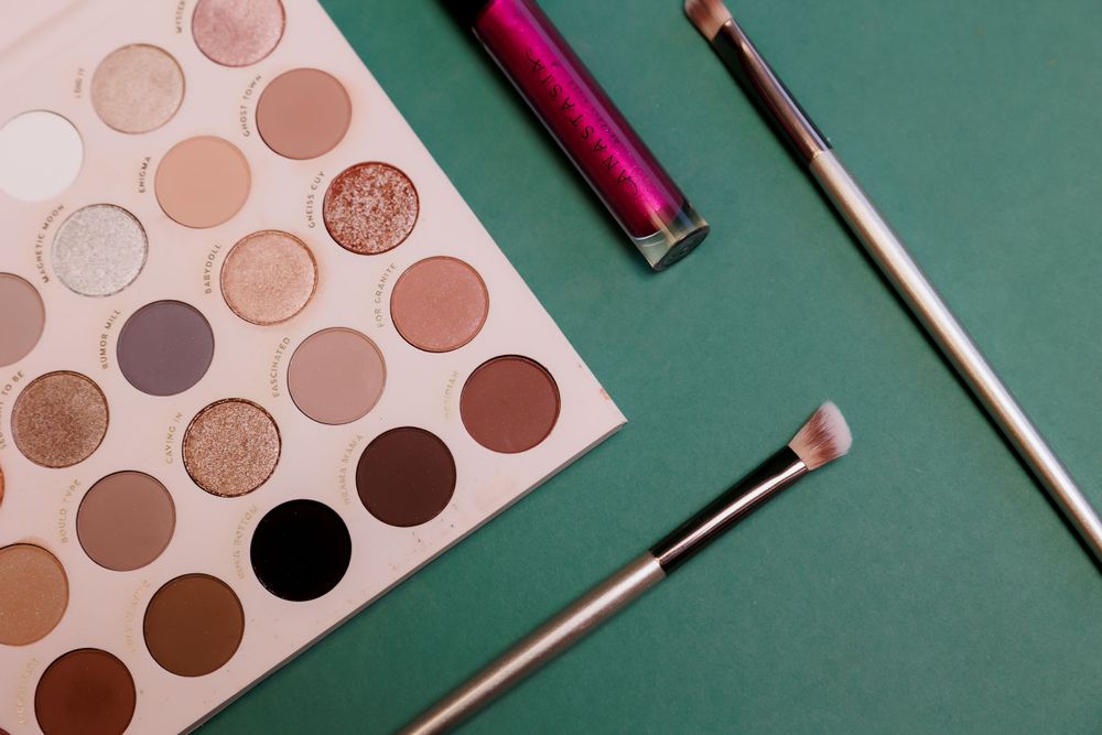 Makeup palette featuring warm neutral tones with brushes and lip product on green surface.