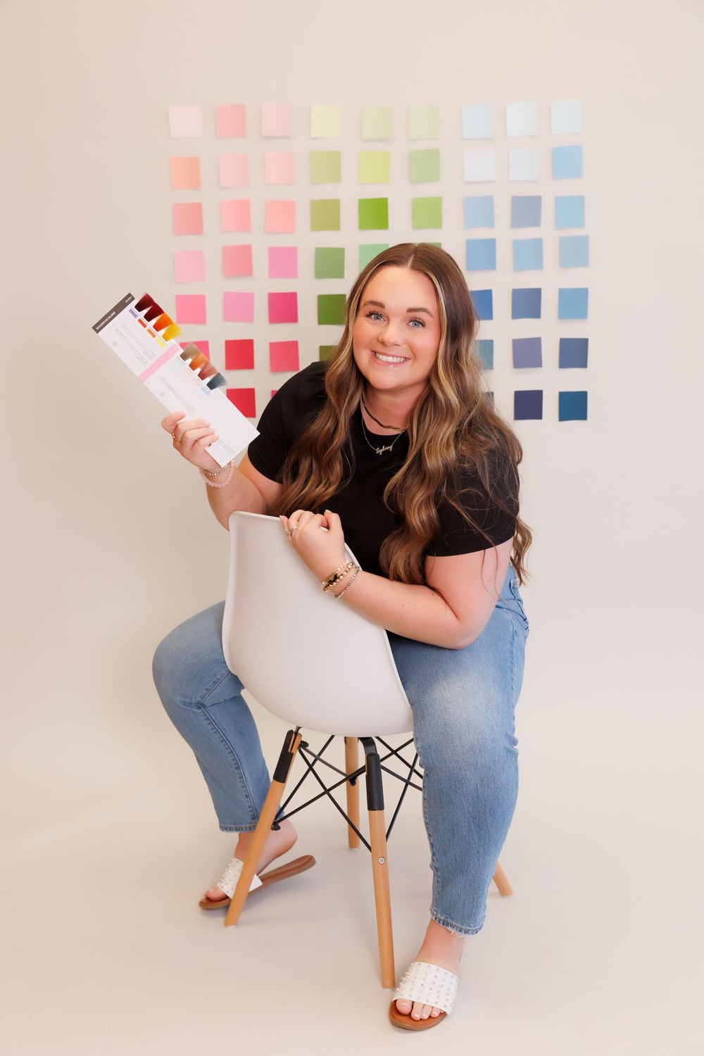 Person sitting on modern chair holding color samples against pastel wall display.