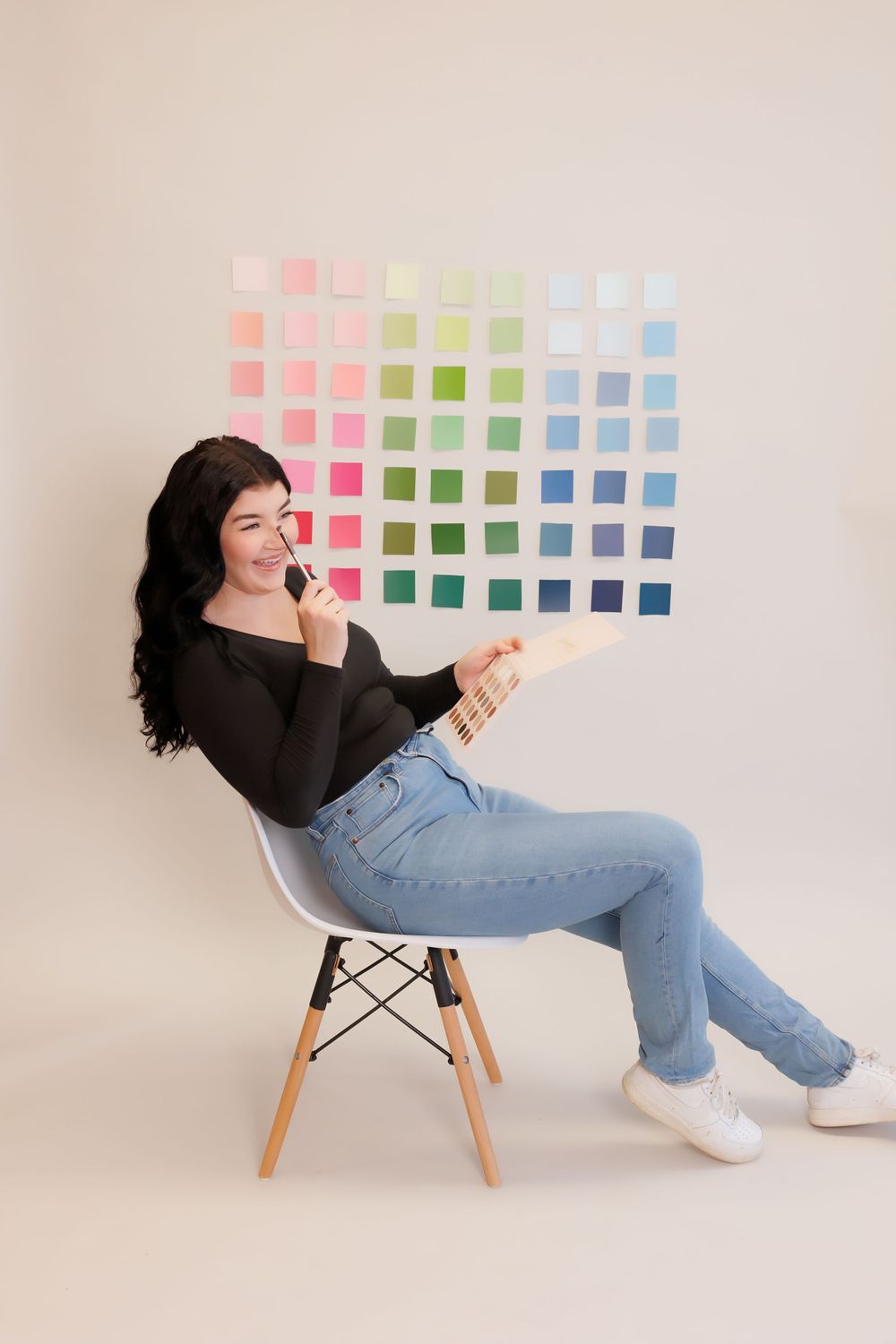 Woman in black top sitting on modern chair against wall with colorful paint swatches.