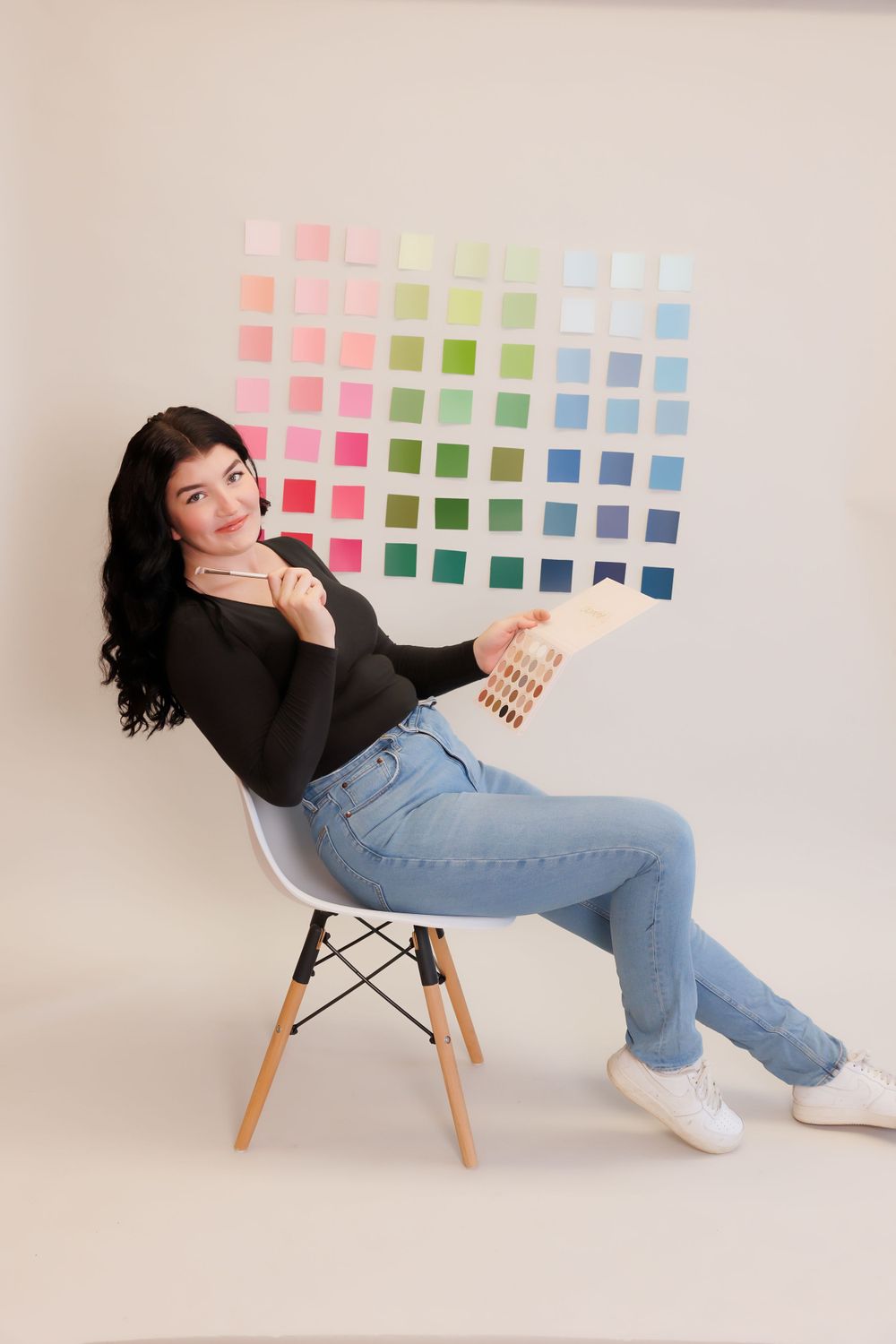 Woman in casual attire displaying color swatches while seated on modern chair.