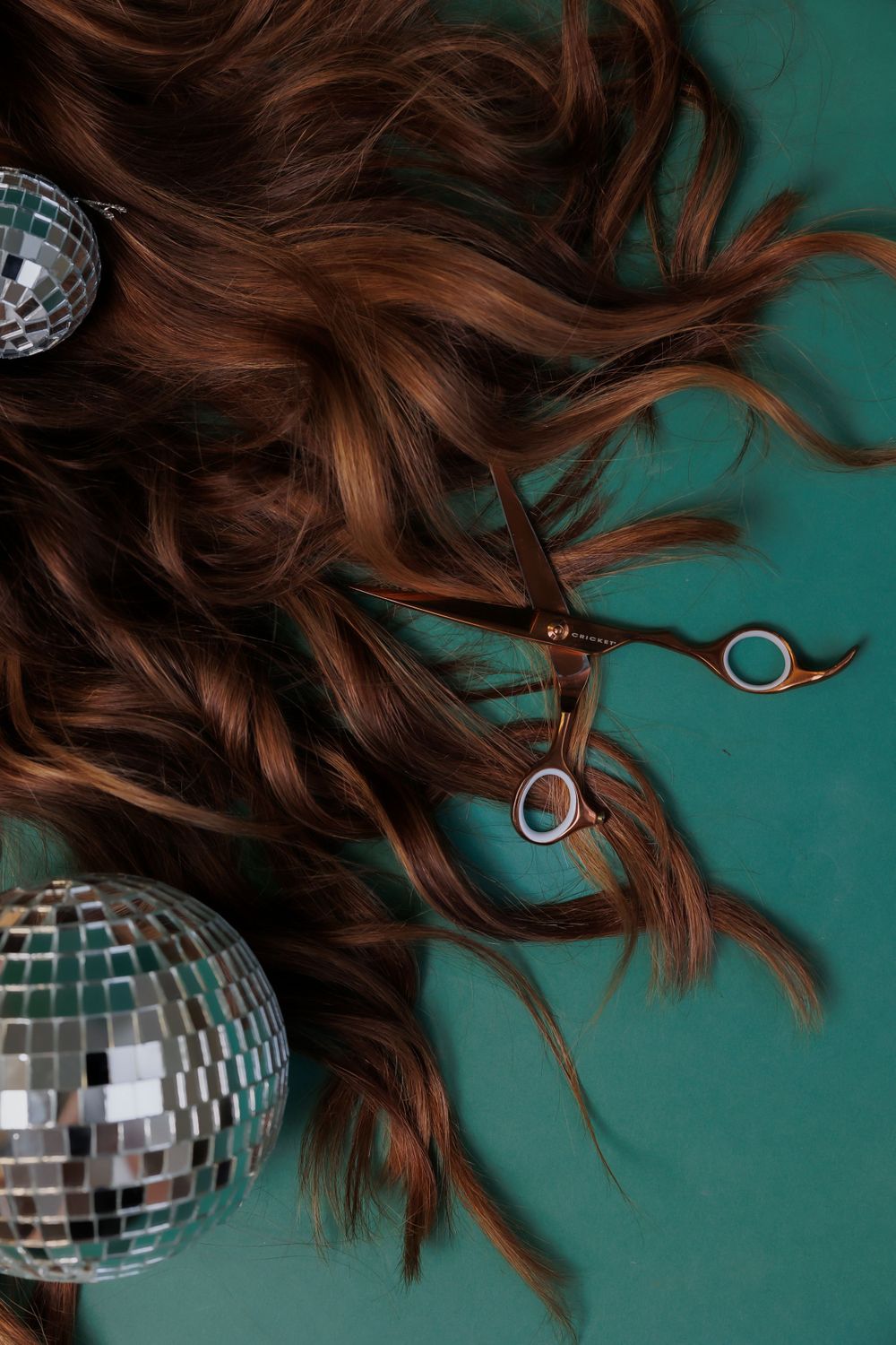 Disco balls and hair styling scissors arranged on teal background.