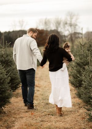 A couple walks hand in hand through a Christmas tree farm on an autumn day.