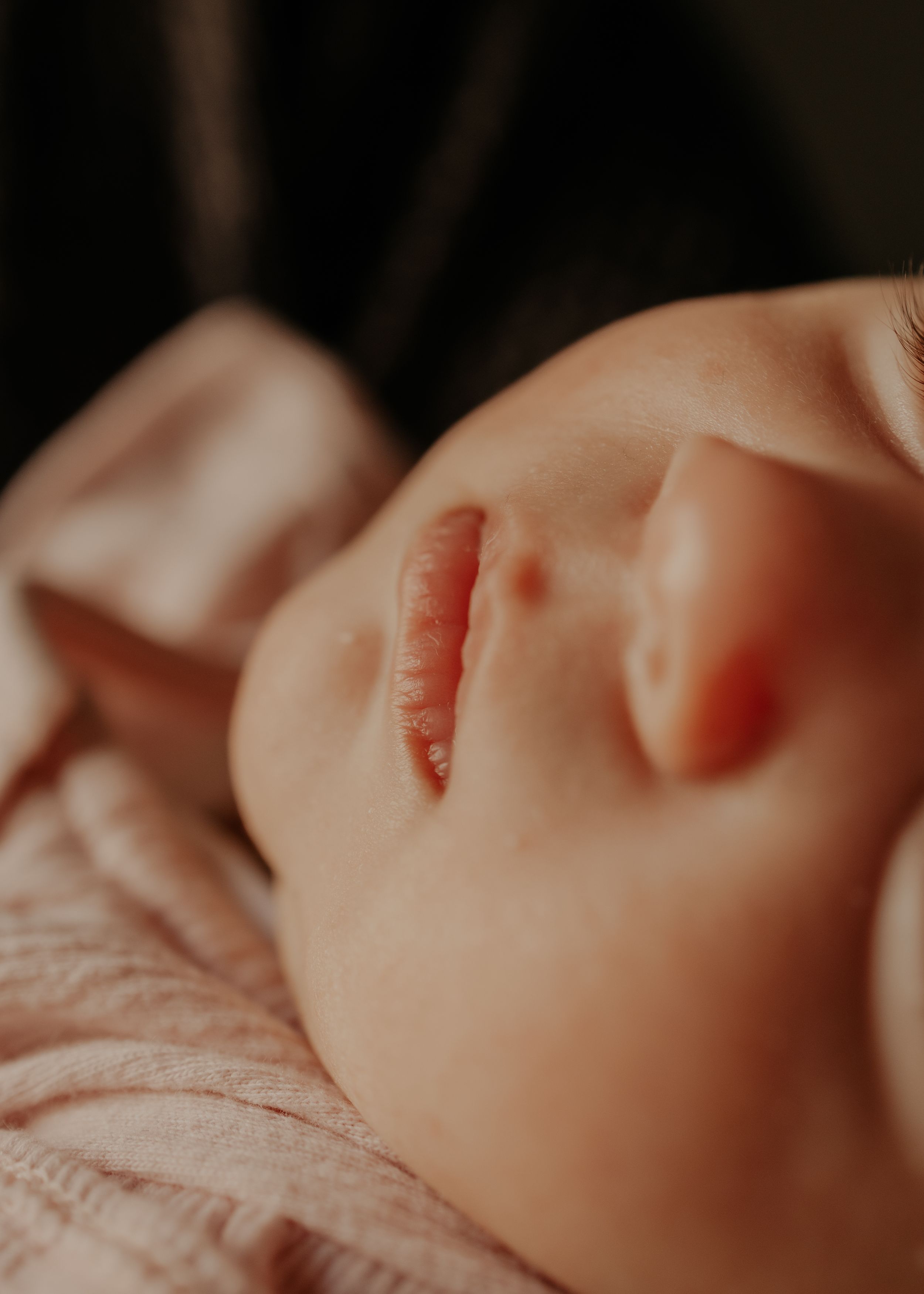 Close-up view of a sleeping baby's face with soft, peachy skin tones in warm lighting.