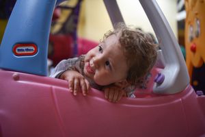 A young child leans out the window of a pink Little Tikes toy car at a birthday party.